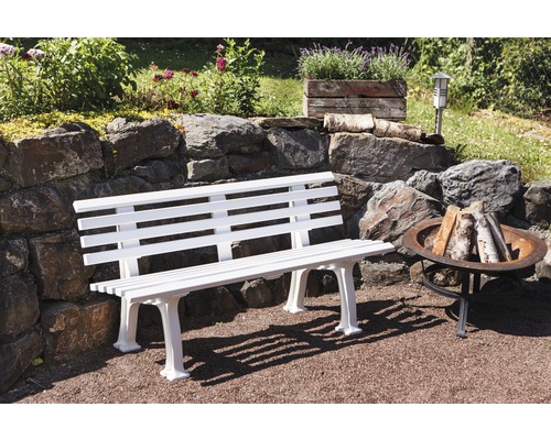 Scène de jardin avec un banc de jardin en bois blanc et un foyer en métal.