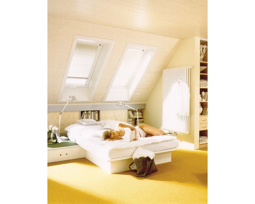 Chambre mansardée lumineuse avec fenêtres de toit, lit et femme