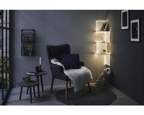 Wohnzimmer mit Sessel, Beistelltischen, beleuchteten Regalen und Dekorationen für eine gemütliche Atmosphäre