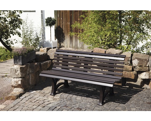 Scène de jardin avec mur en pierre et un banc de jardin en métal.