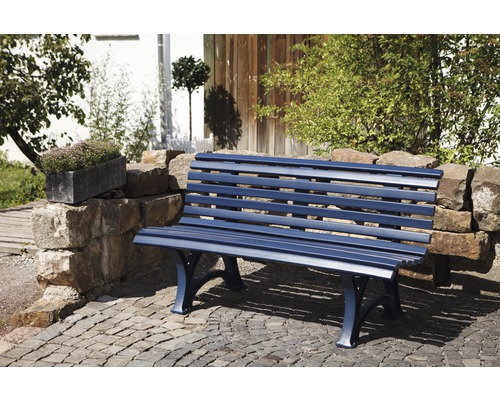 Banc de jardin bleu en métal sur sol pavé devant un mur de pierre