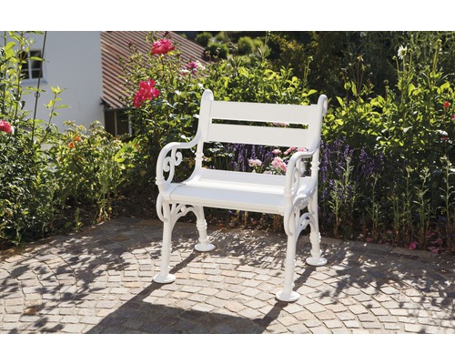 Banc de jardin blanc en métal sur une zone pavée devant des buissons et des fleurs