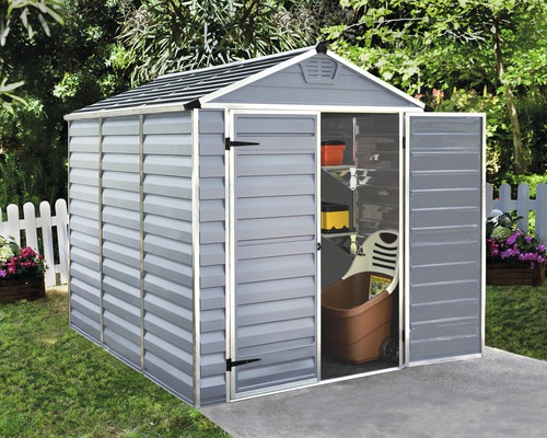 Abri de jardin gris avec porte ouverte dans le jardin, contenant une brouette et des étagères