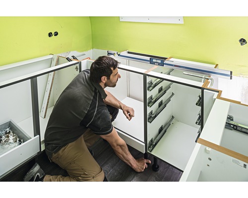 Un homme assemble des éléments bas de cuisine avec tiroirs et pieds réglables.