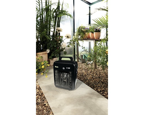 Gewächshaus mit Pflanzen und einem schwarzen Heizlüfter mit 2 Kilowatt Leistung