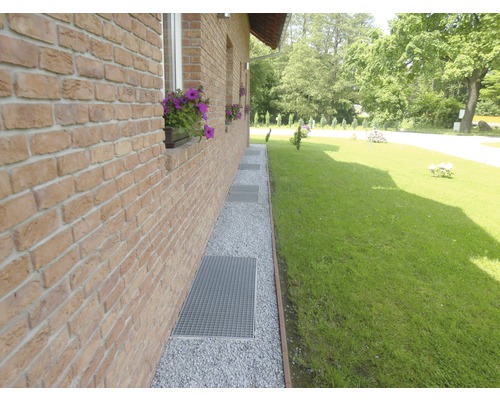 Extérieur d''une maison avec mur en briques, chemin de gravier et grilles métalliques devant les fenêtres