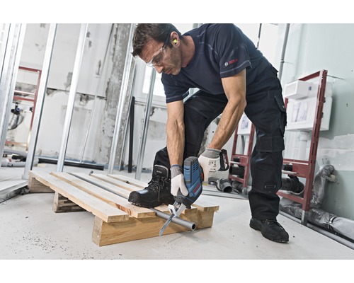 Un homme coupe un tuyau avec une scie sabre sur une palette en bois sur un chantier.