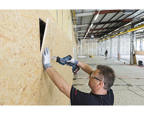 Un artisan scie un trou dans une plaque de bois avec une scie sabre sans fil.