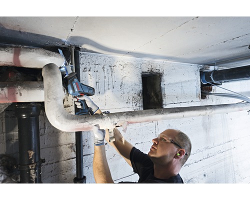 Un homme scie un tuyau dans une cave avec une scie sabre sans fil.