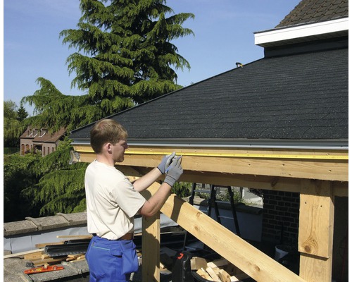 Ein Mann misst eine Holzkonstruktion mit einem Rollmeter.