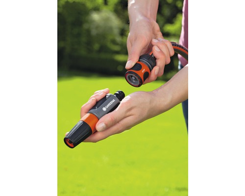 Une personne connecte une lance d''arrosage à un raccord de tuyau Gardena.