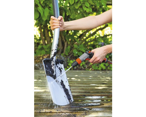 Eine Person reinigt eine Schaufel mit einem Wasserstrahl auf einer Holzoberfläche.