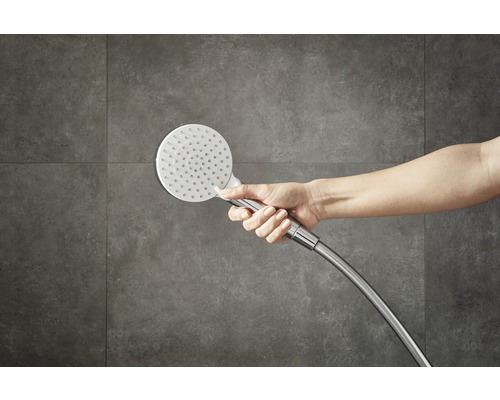 Hand hält Handbrause vor einer Wand