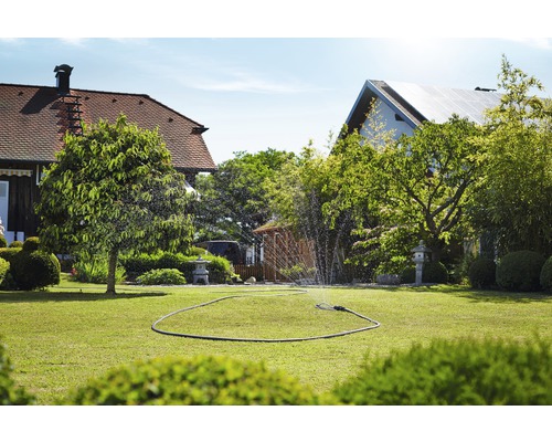 Bewässerter Rasen mit Rasensprenger in einem Garten.
