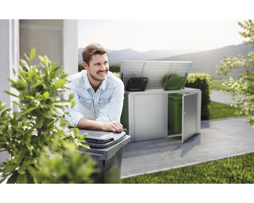 Scène avec un homme appuyé contre une poubelle et un abri poubelle en arrière-plan.