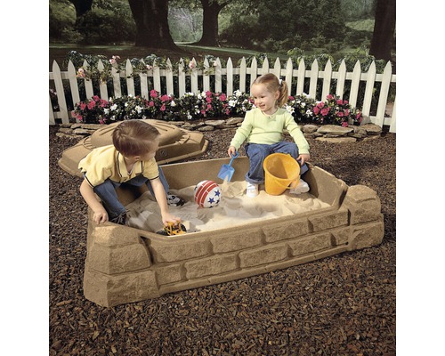 Bac à sable avec deux enfants, des jouets de sable et un couvercle dans le jardin.