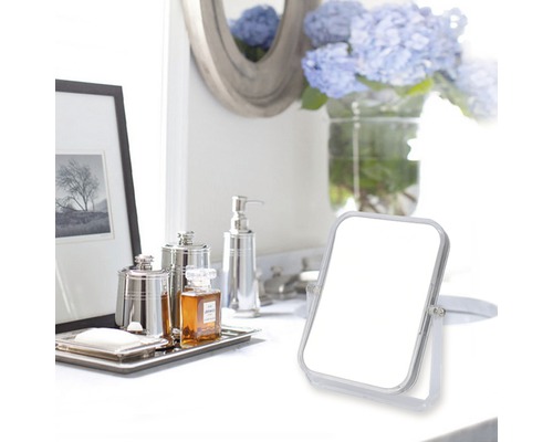 Badezimmerszene mit Kosmetikspiegel, Seifenspender und Dekorationsgegenständen auf einer weißen Oberfläche