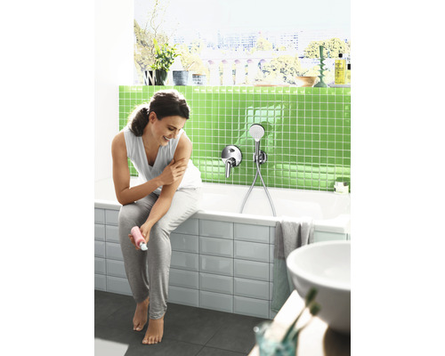 Salle de bains lumineuse avec baignoire, robinetterie et femme s''hydratant le corps.
