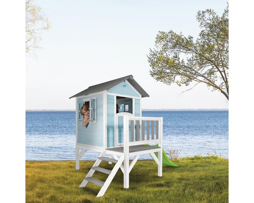 Maisonnette avec toboggan, escalier et fenêtre sur une pelouse devant un lac