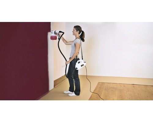 Femme peignant un mur avec un système de pulvérisation de peinture dans une pièce