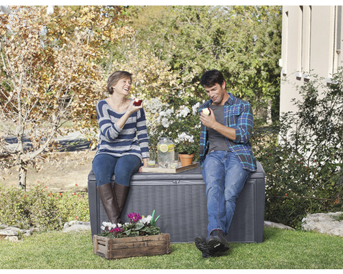 Ein Paar sitzt auf einer grauen Gartenbox im Freien und isst Äpfel.