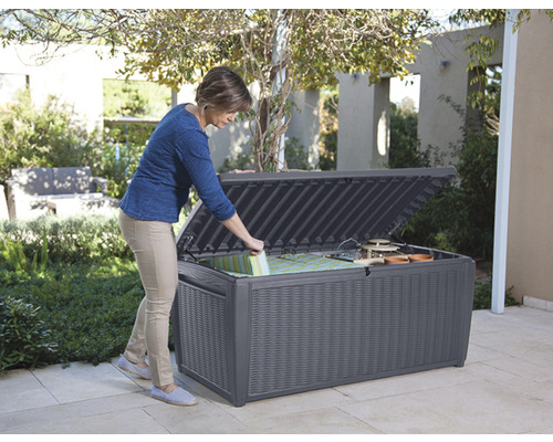 Frau öffnet graue Gartenbox zur Aufbewahrung von Gartengeräten und Kissen im Freien.