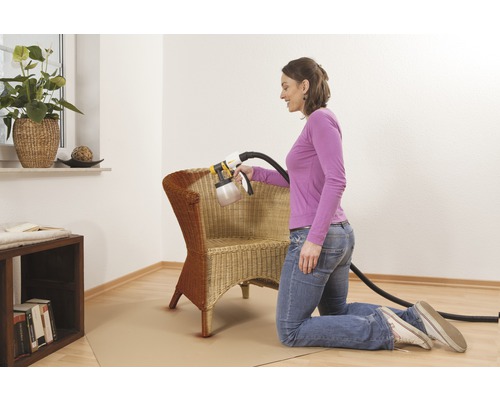 Femme vernit un fauteuil en osier avec un système de pulvérisation de peinture