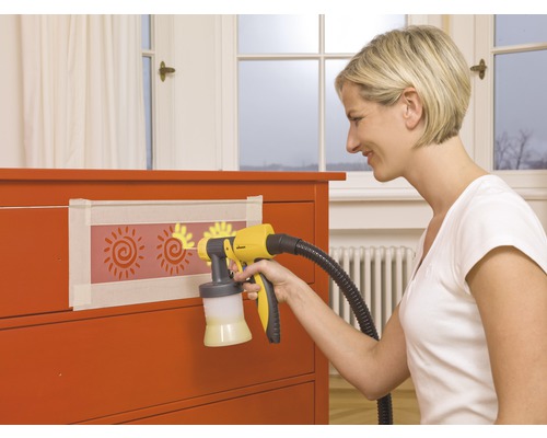 Femme utilisant un pistolet à peinture sur une commode avec des pochoirs de soleil