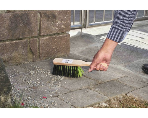 Une personne utilise une balayette à manche en bois pour nettoyer le pavage.