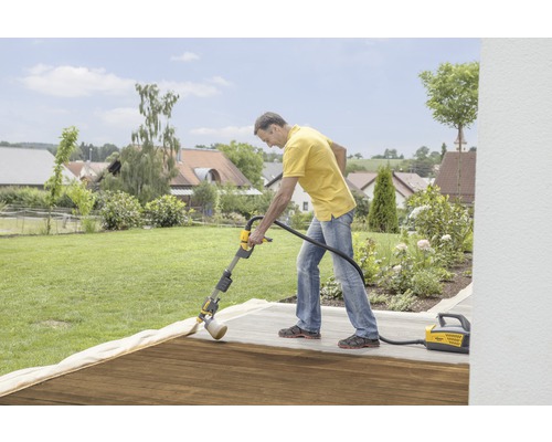 Ein Mann behandelt eine Holzterrasse mit einem Farbsprühsystem von Wagner im Garten.