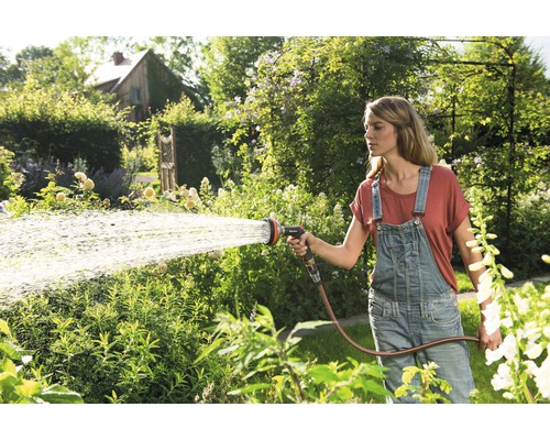 Frau bewässert Garten mit Gartenschlauch und Sprühkopf