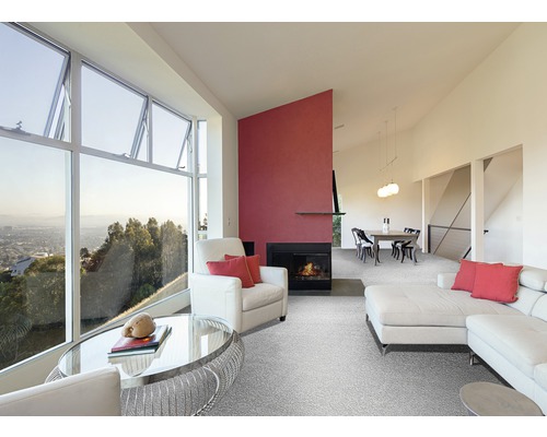 Salon avec grande fenêtre, fauteuil, canapé, tapis et cheminée.