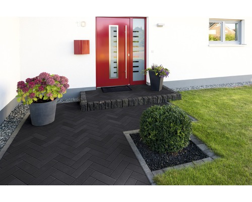 Eingangsbereich eines Hauses mit dunklen Pflastersteinen, Blumen und einem gepflegten Garten