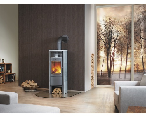 Salon avec poêle à bois, bois de chauffage et fenêtre avec paysage hivernal