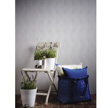 Scène décorative avec des pots de fleurs sur une chaise pliante devant un papier peint à motifs et un panier tressé avec des coussins.