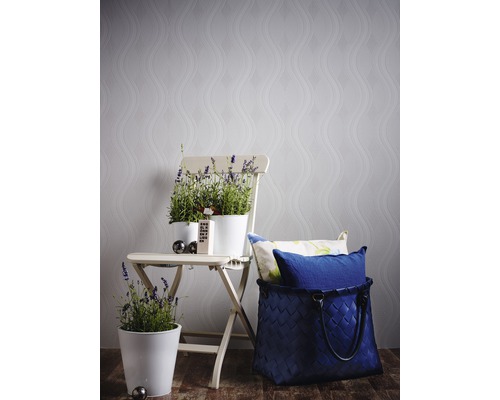 Scène décorative avec des pots de fleurs sur une chaise pliante devant un papier peint à motifs et un panier tressé avec des coussins.