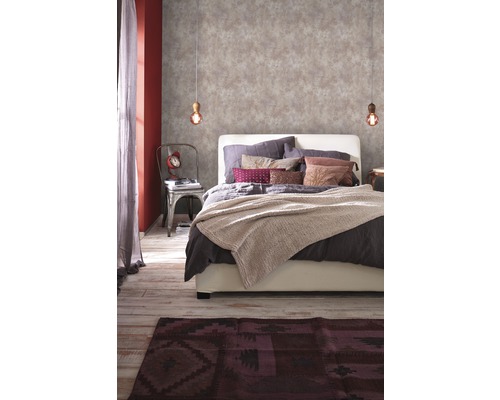 Chambre avec papier peint à motifs, lit, tapis et éléments décoratifs pour une ambiance chaleureuse.