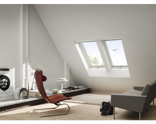 Chambre mansardée lumineuse avec fenêtres de toit, fauteuil et canapé