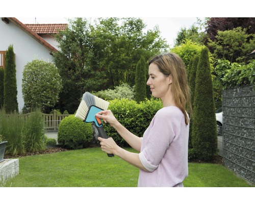 Frau hält Bürste zur Reinigung von Oberflächen im Garten