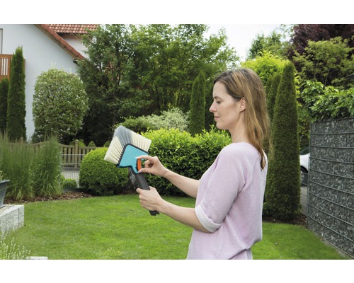 Frau betrachtet eine Flächenbürste im Garten.