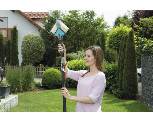 Frau benutzt eine Waschbürste mit Teleskopstiel zur Reinigung im Garten.