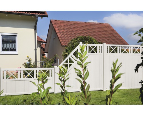 Vue de jardin avec clôture blanche et portail devant des maisons.