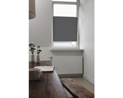 Innenaufnahme eines Zimmers mit einem grauen Plissee am Fenster, einem Holztisch und einer Sitzbank