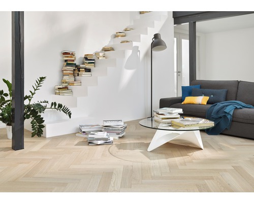 Salon avec parquet clair à chevrons, escalier avec livres et canapé gris