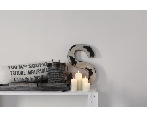 Scène décorative avec coussin, boîte, bougies et ornement de lettre sur une étagère blanche.