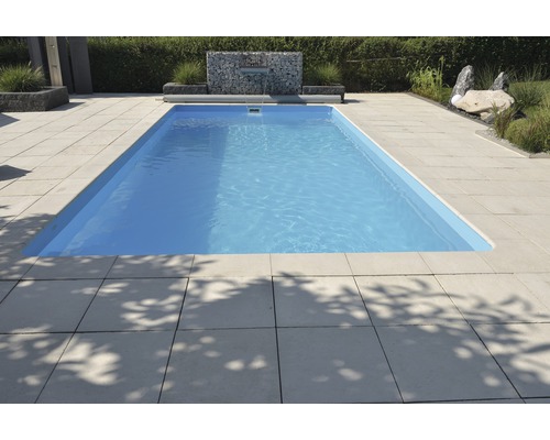 Piscine rectangulaire entourée de dalles de pierre dans le jardin