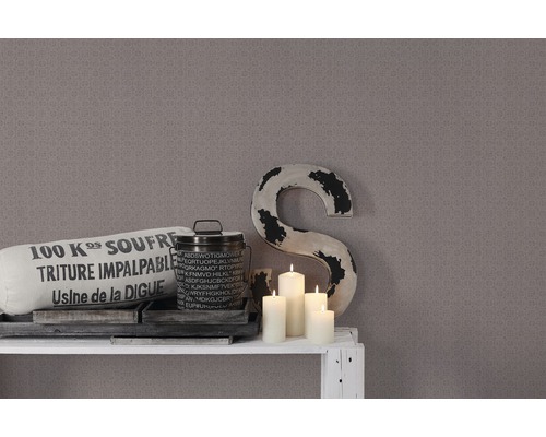 Dekorative Szene mit Kissen, Dose, Kerzen und einer grossen Buchstaben-Skulptur vor einer gemusterten Wand.