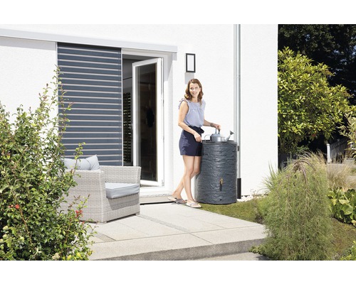 Frau giesst Pflanzen mit Regenwasser aus einer Regentonne im Garten.