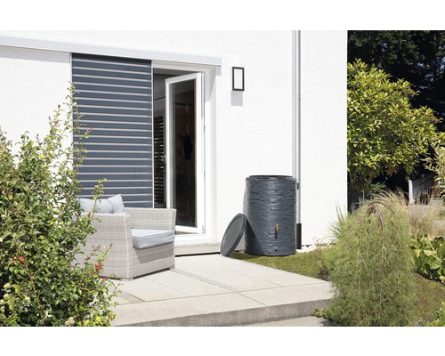 Regentonne auf einer Terrasse neben einem Haus mit Garten