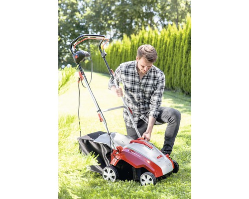 Un homme utilise un scarificateur dans le jardin. L''appareil est équipé d''un bac de ramassage.